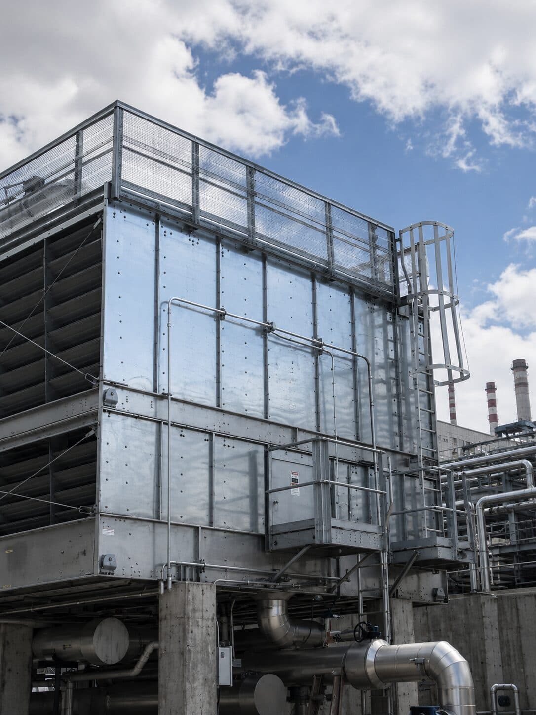 Industrial cooling tower with pipes and chimneys in the background.