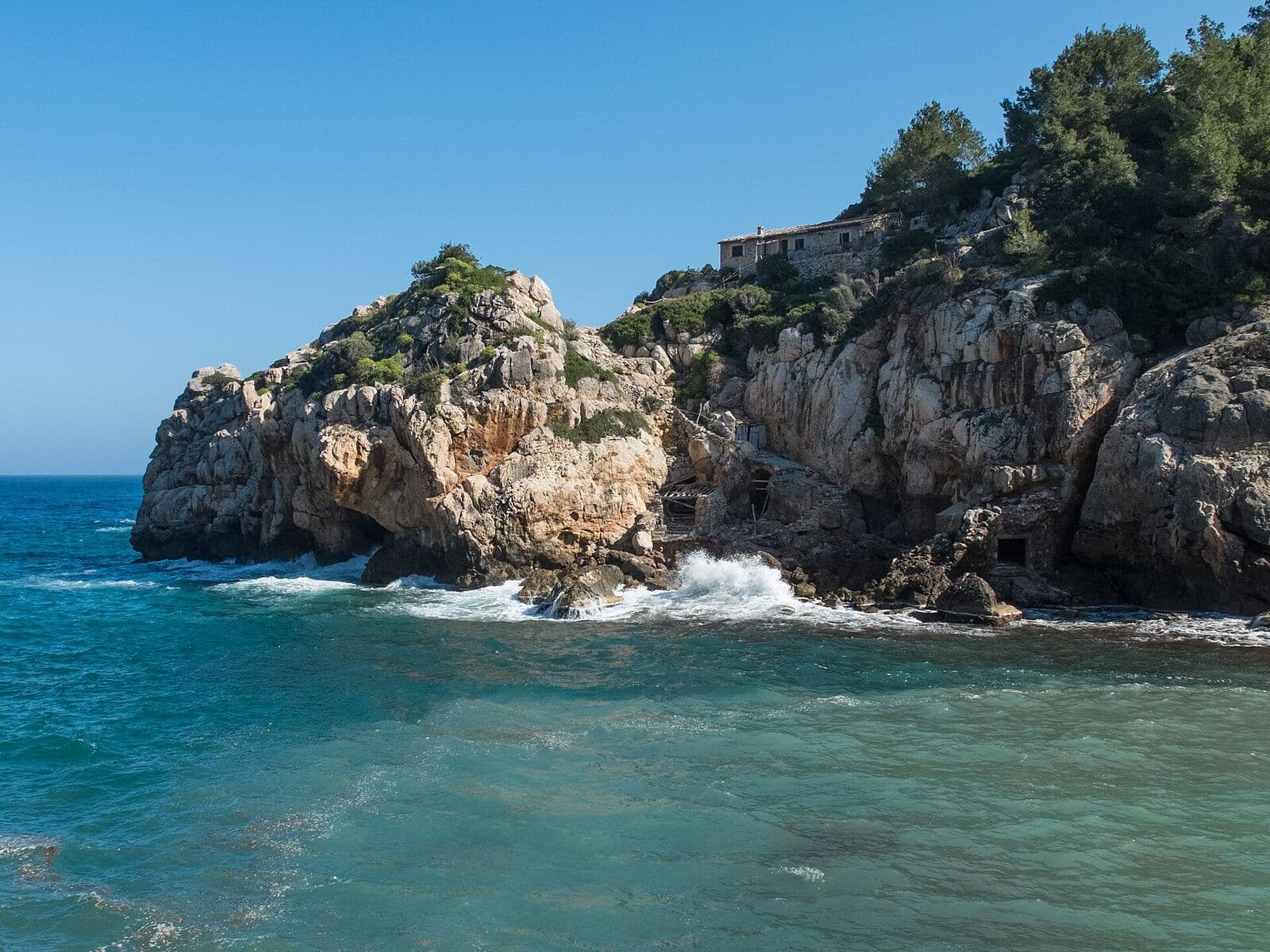 Cala Deià, com grandes rochas, água turquesa e falésias cobertas de vegetação