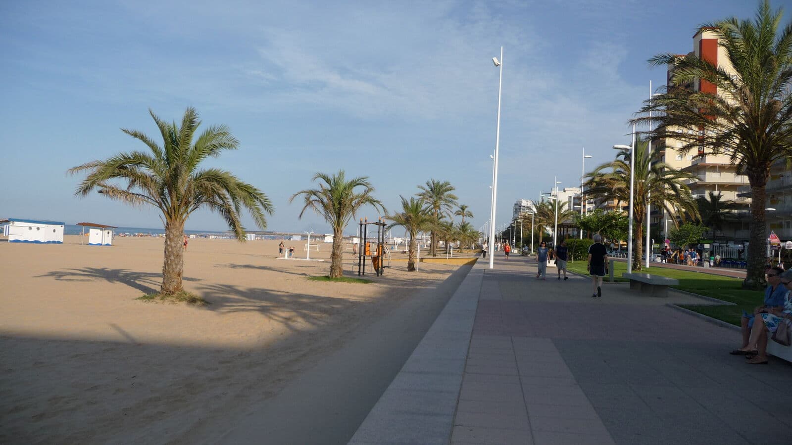 The Playa de Gandia seafront promenade in the early evening, with palm trees, the sand on the left and apartment blocks in the distance