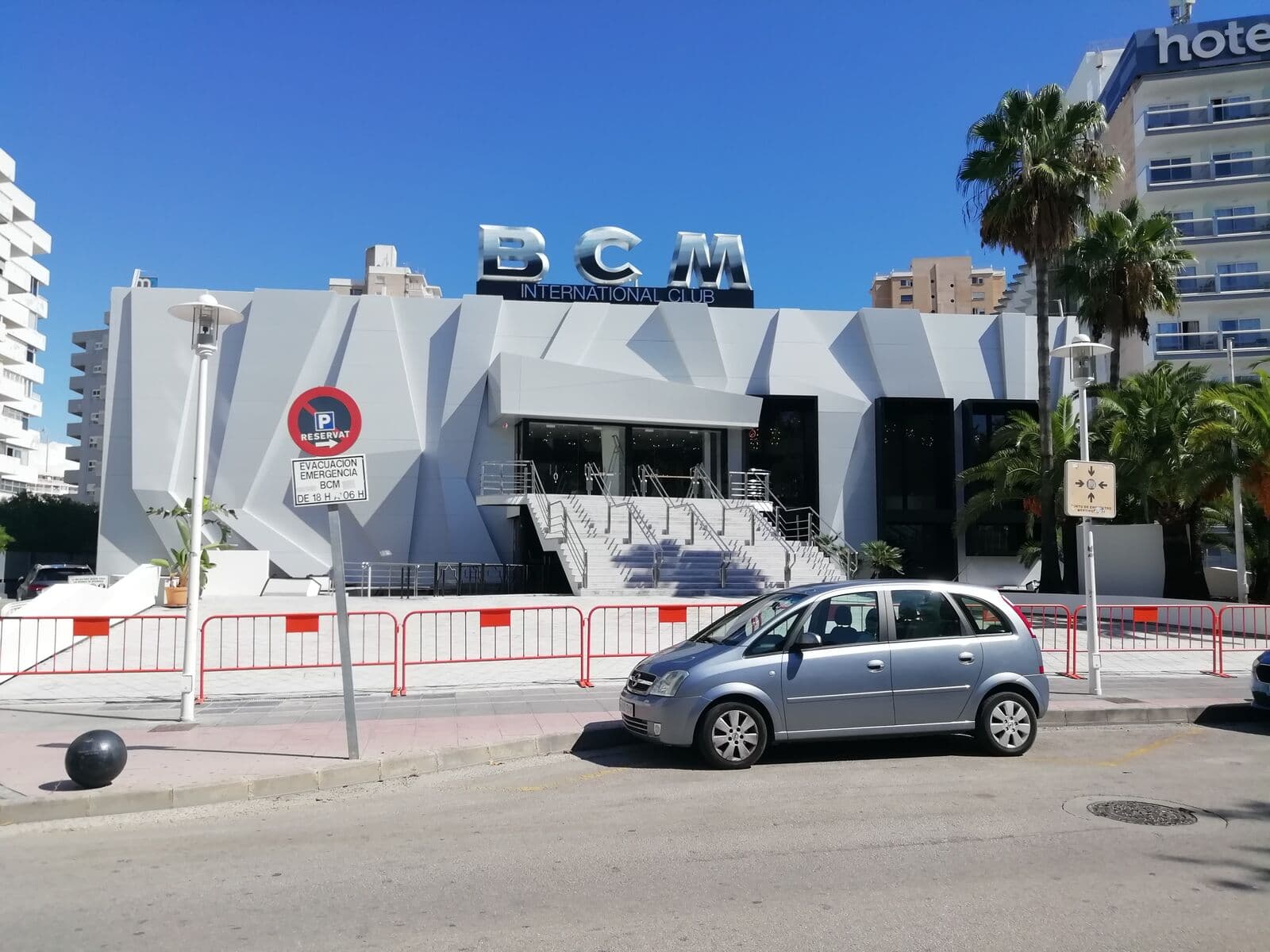 Facciata bianca della discoteca BCM a Magaluf, con l'insegna, palme e un hotel accanto