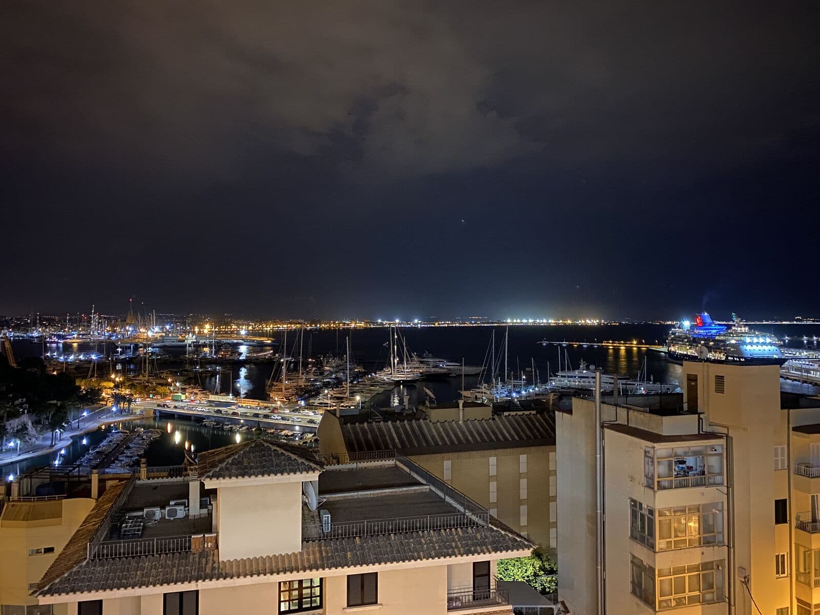 Il porto di Palma di notte, con barche ormeggiate, edifici illuminati e le luci della baia sullo sfondo
