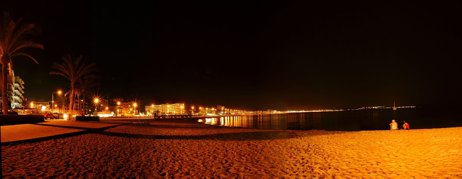 Panorama notturno della Playa de Palma, con la sabbia illuminata e le luci del lungomare e degli hotel lungo la costa