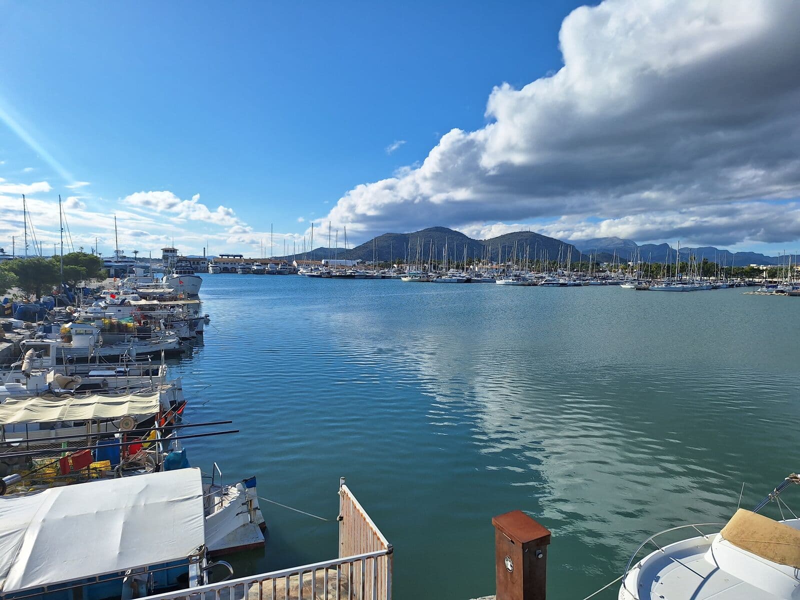 Il porto di Alcúdia con barche ormeggiate e montagne sullo sfondo sotto un cielo nuvoloso