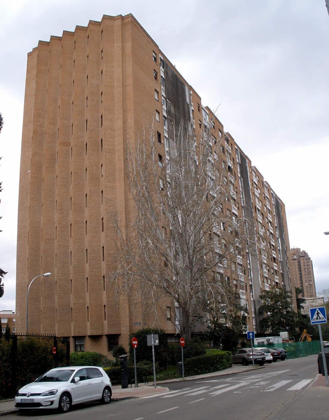 Backstein-Apartmenthaus in der Calle Samaria in Madrid, von der Straße aus gesehen, mit Bäumen und Fahrzeugen im Vordergrund.