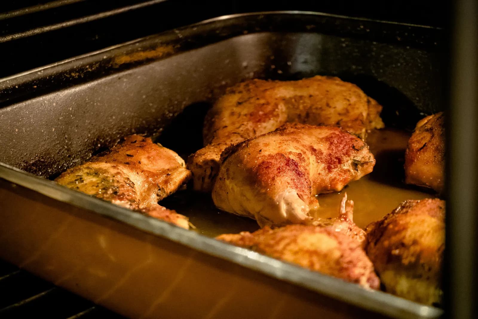 Spiced, golden chicken legs roasting in a metal tray inside the oven.