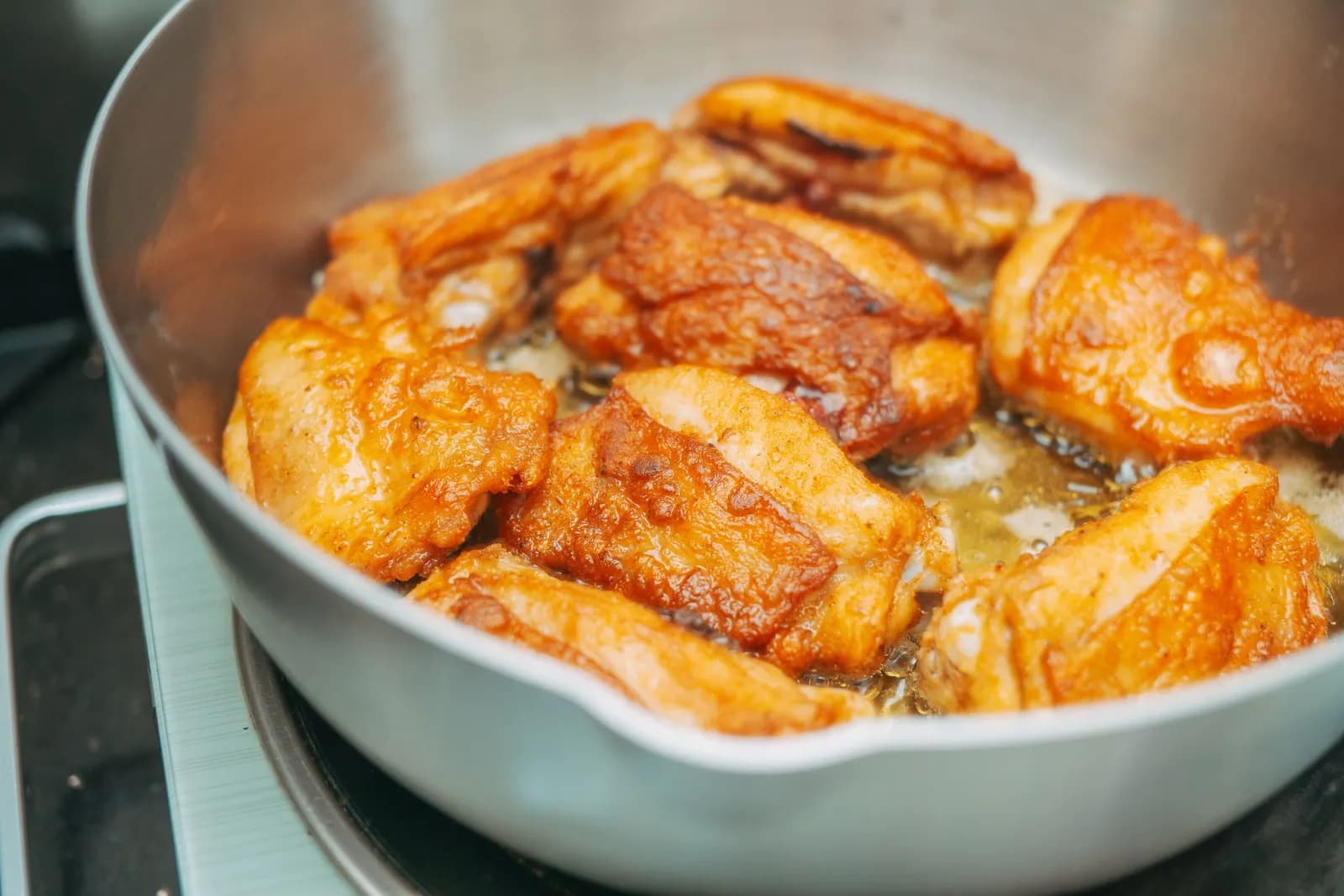 Chicken thighs with golden skin cooking in a large frying pan on the hob.