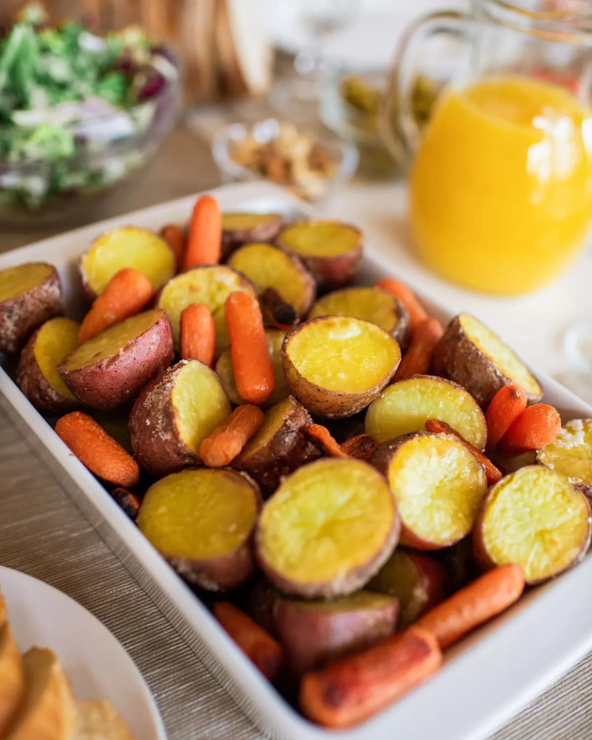 White rectangular dish of halved potatoes and small roast carrots, golden at the edges.