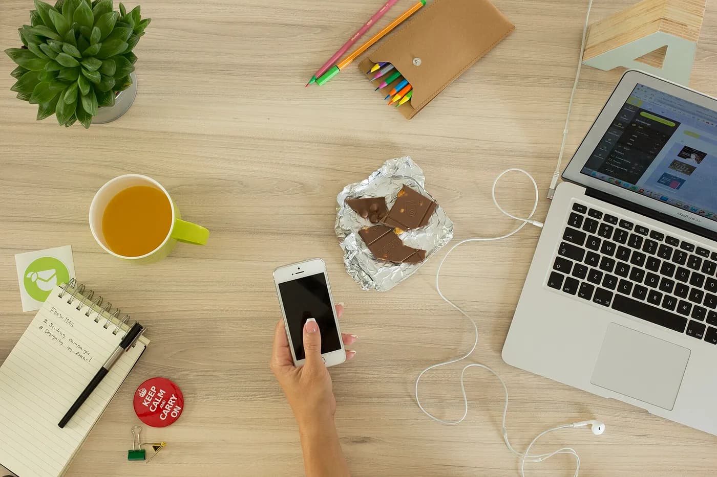 A phone and notebook lie among a laptop, tea and other everyday objects on a desk.