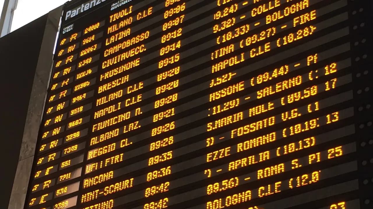 Departures board at an Italian railway station showing destinations and times in orange letters.