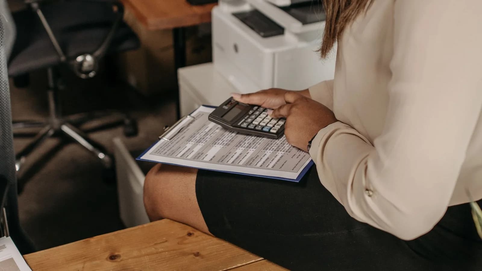 Pessoa a consultar documentos e a utilizar uma calculadora numa secretária.