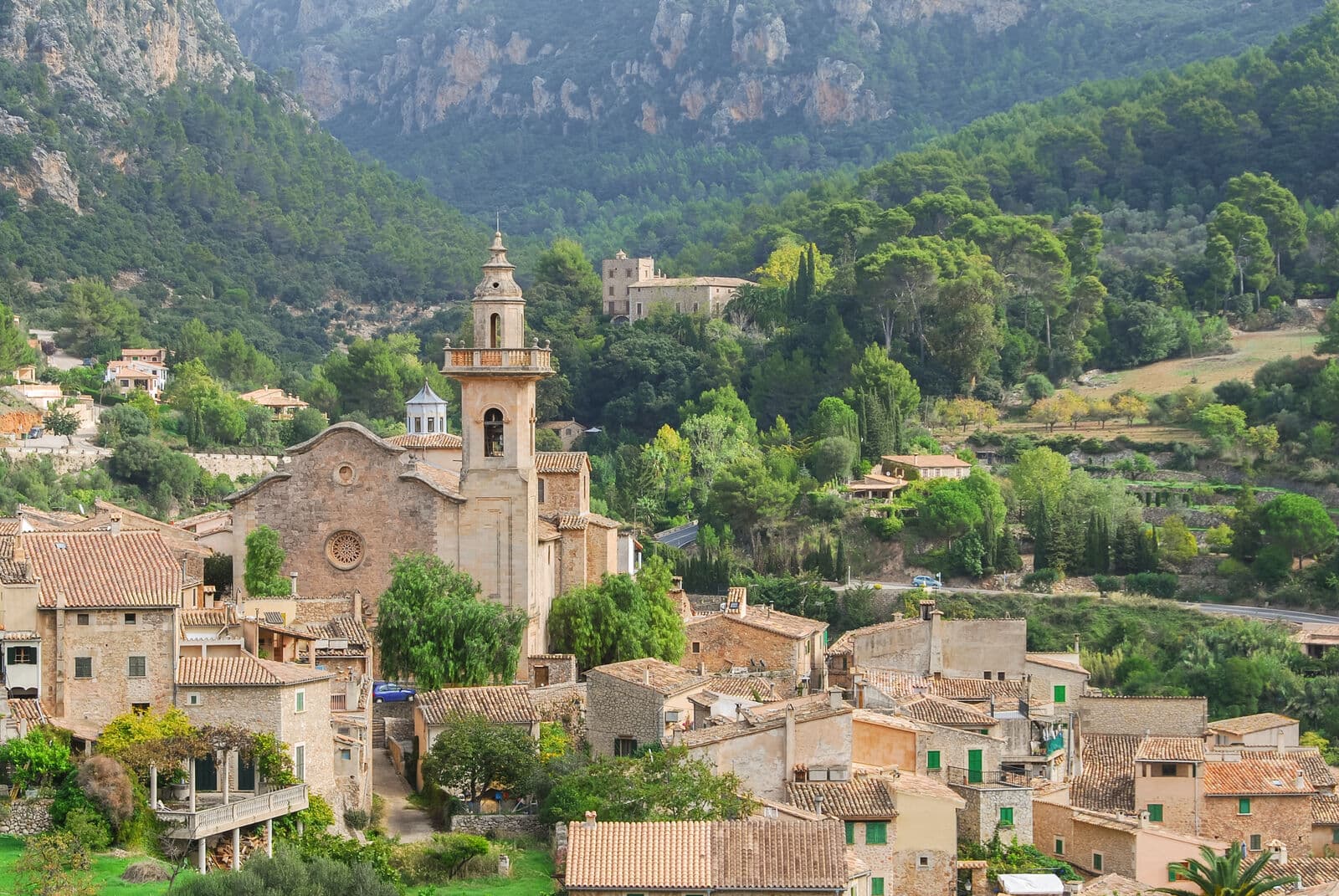 Casas de pedra de Valldemossa com o campanário da igreja, cercadas de árvores e montanhas