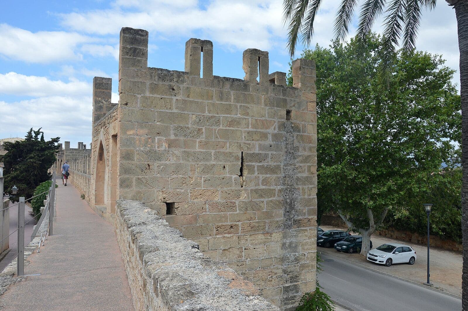 A walkway on top of Alcúdia's medieval wall, with a crenellated tower and trees beside the street