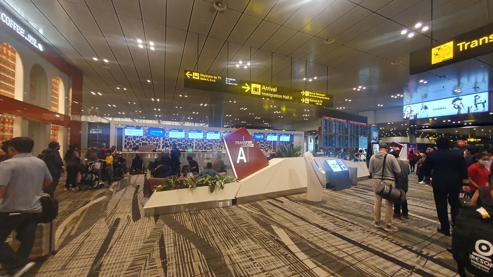 Transferbereich im Terminal 3 des Flughafens Singapur-Changi mit Transferschaltern, Fluginformationsbildschirmen und Reisenden mit Gepäck.