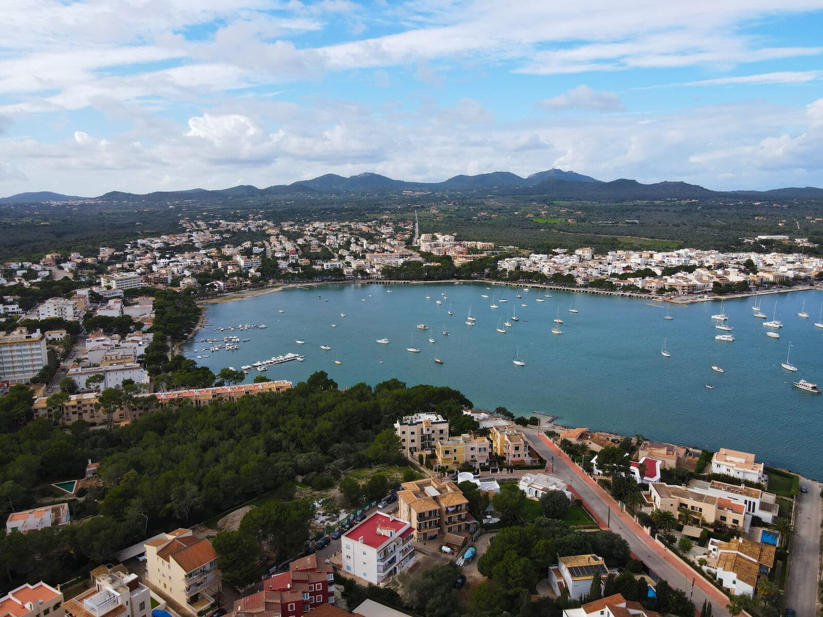 Vista aérea da baía de Portocolom, com barcos ancorados, casas baixas e as colinas ao fundo