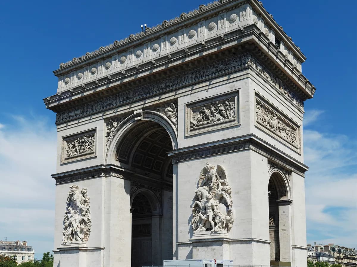 The Arc de Triomphe de l’Étoile in Paris, with its carved reliefs, under a blue sky.