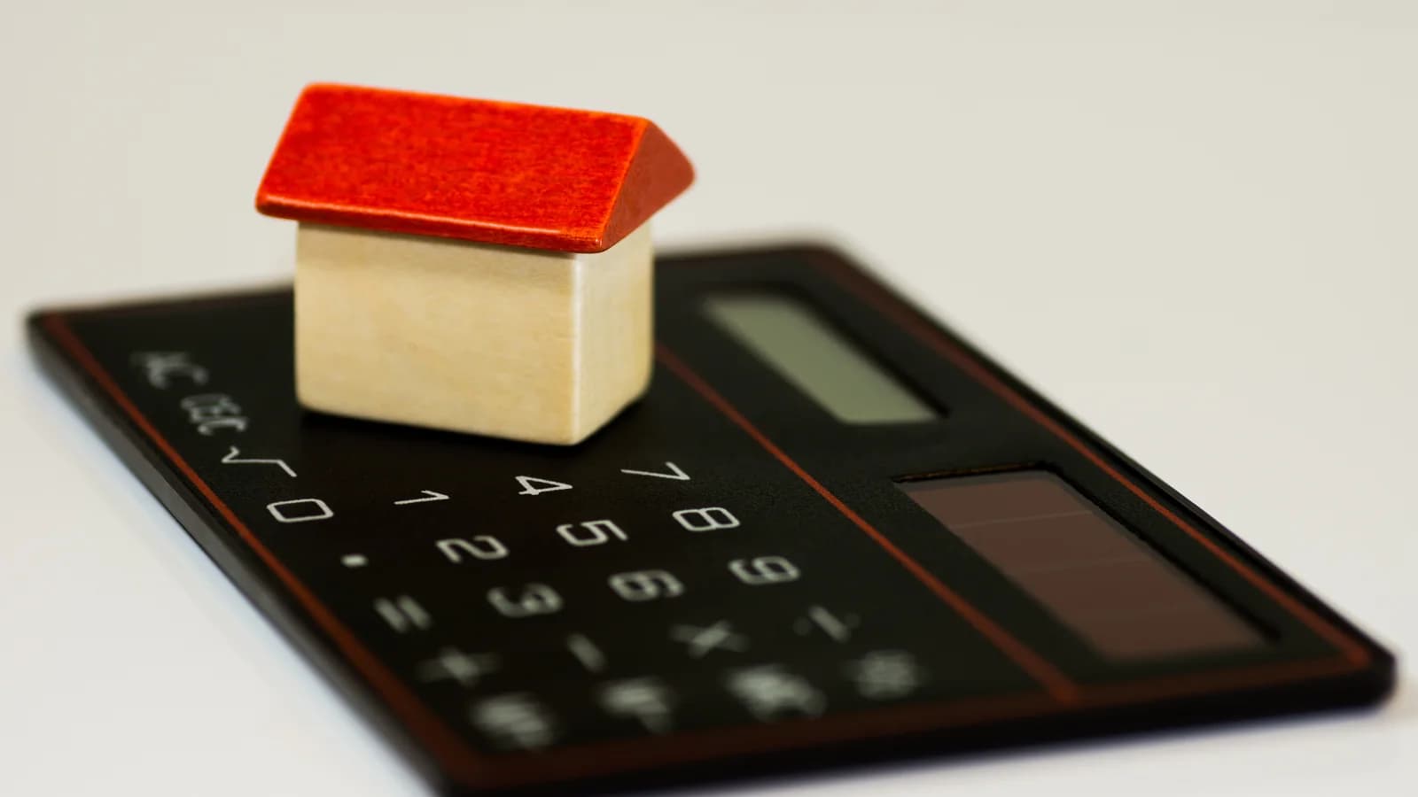 A small model house resting on a calculator, used as an illustration of household budgeting.