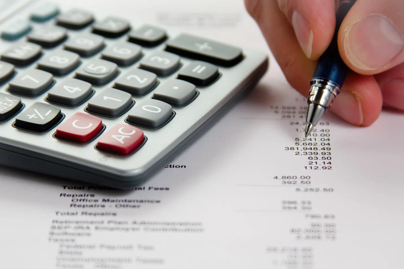 Close-up of a hand using a calculator beside a pen and printed financial statement.