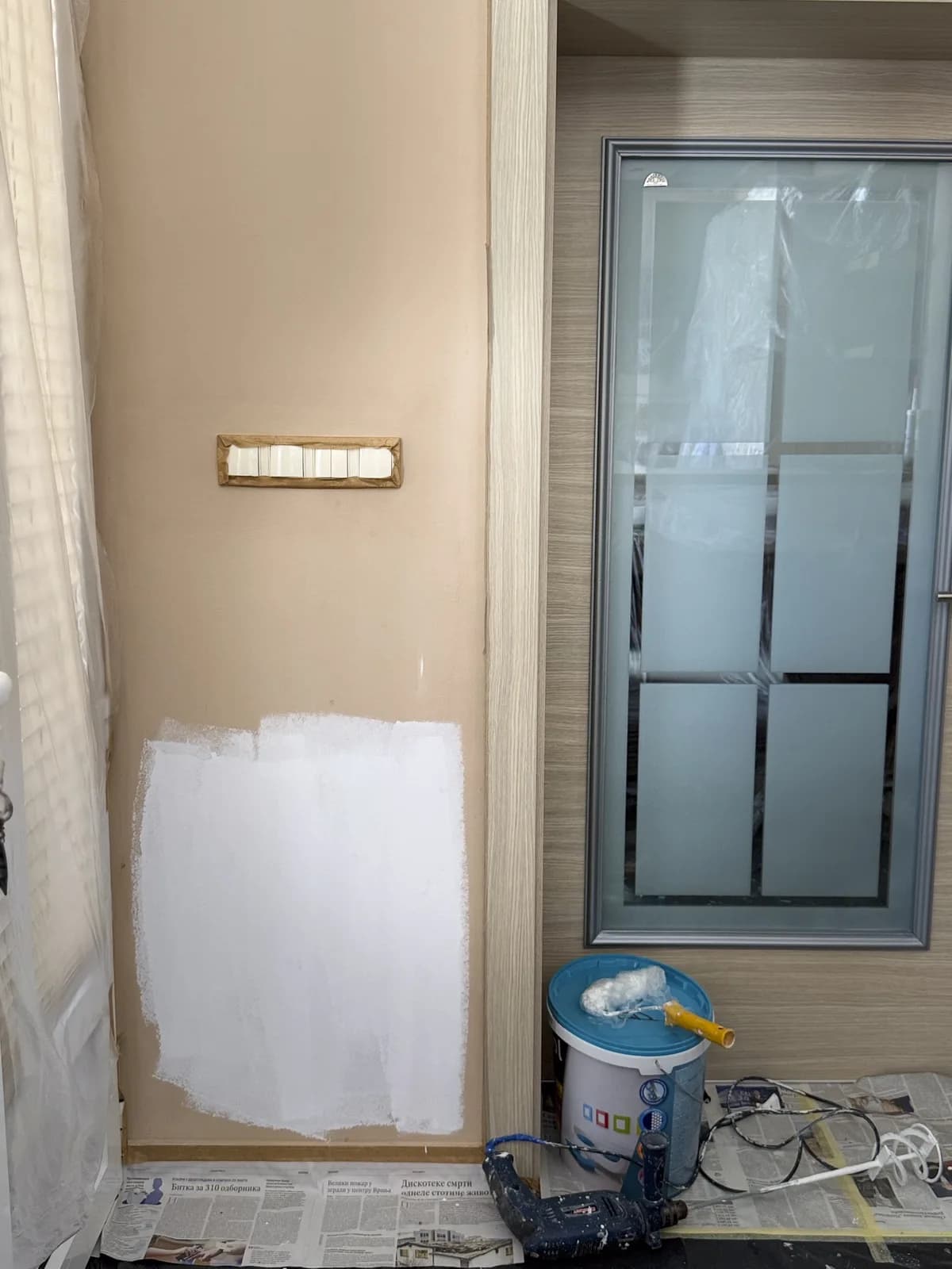 Interior wall with one area newly painted, another unfinished, and painting tools on the floor.
