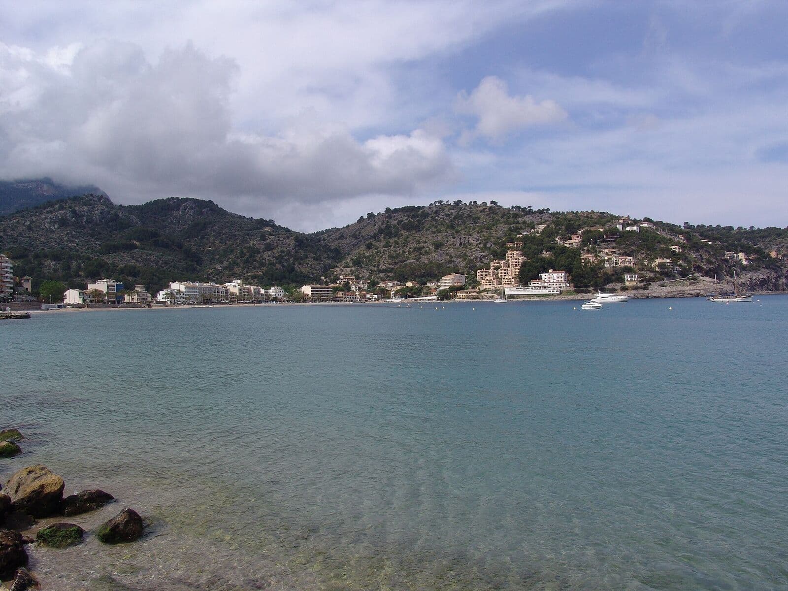 A baía de Port de Sóller com água calma, casas na margem e montanhas ao fundo