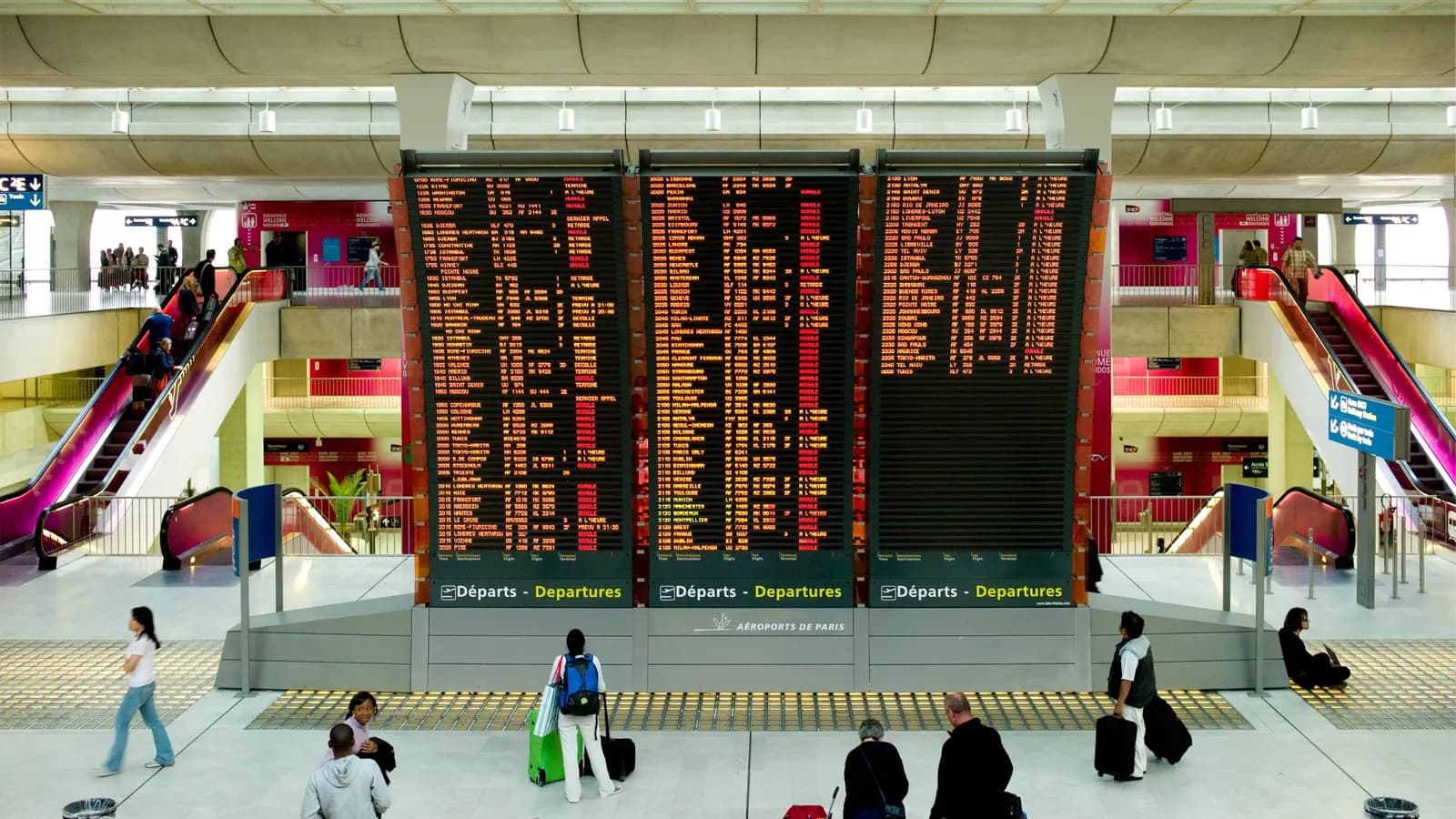 Paneles de salidas del aeropuerto de París-Charles de Gaulle con numerosos vuelos cancelados y pasajeros con maletas en el vestíbulo.