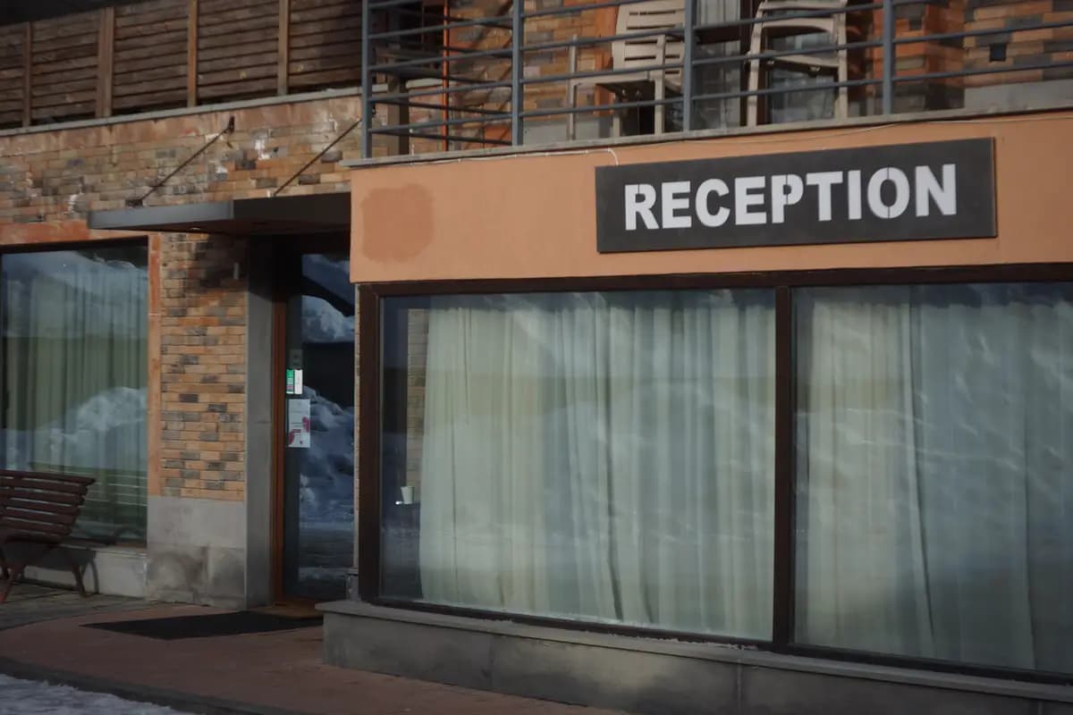 Fachada de un alojamiento con un cartel que dice «RECEPTION» sobre una ventana con cortinas y nieve en el exterior.
