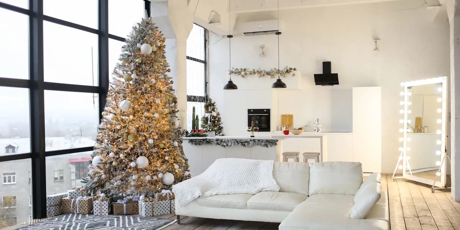 Sala luminosa com uma árvore de Natal nevada decorada com bolas brancas e douradas e luzes quentes, presentes na base e um sofá branco ao lado.