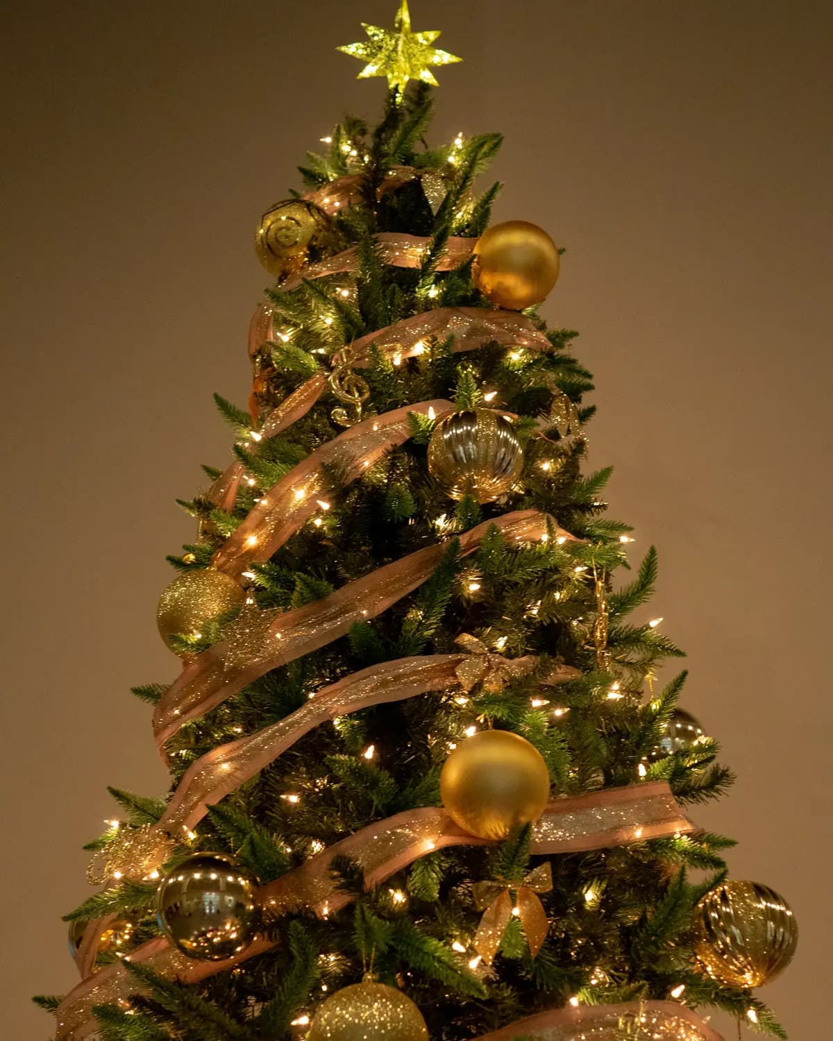 Árvore de Natal envolvida em espiral por uma fita dourada, com bolas douradas, luzes quentes e uma estrela no topo.