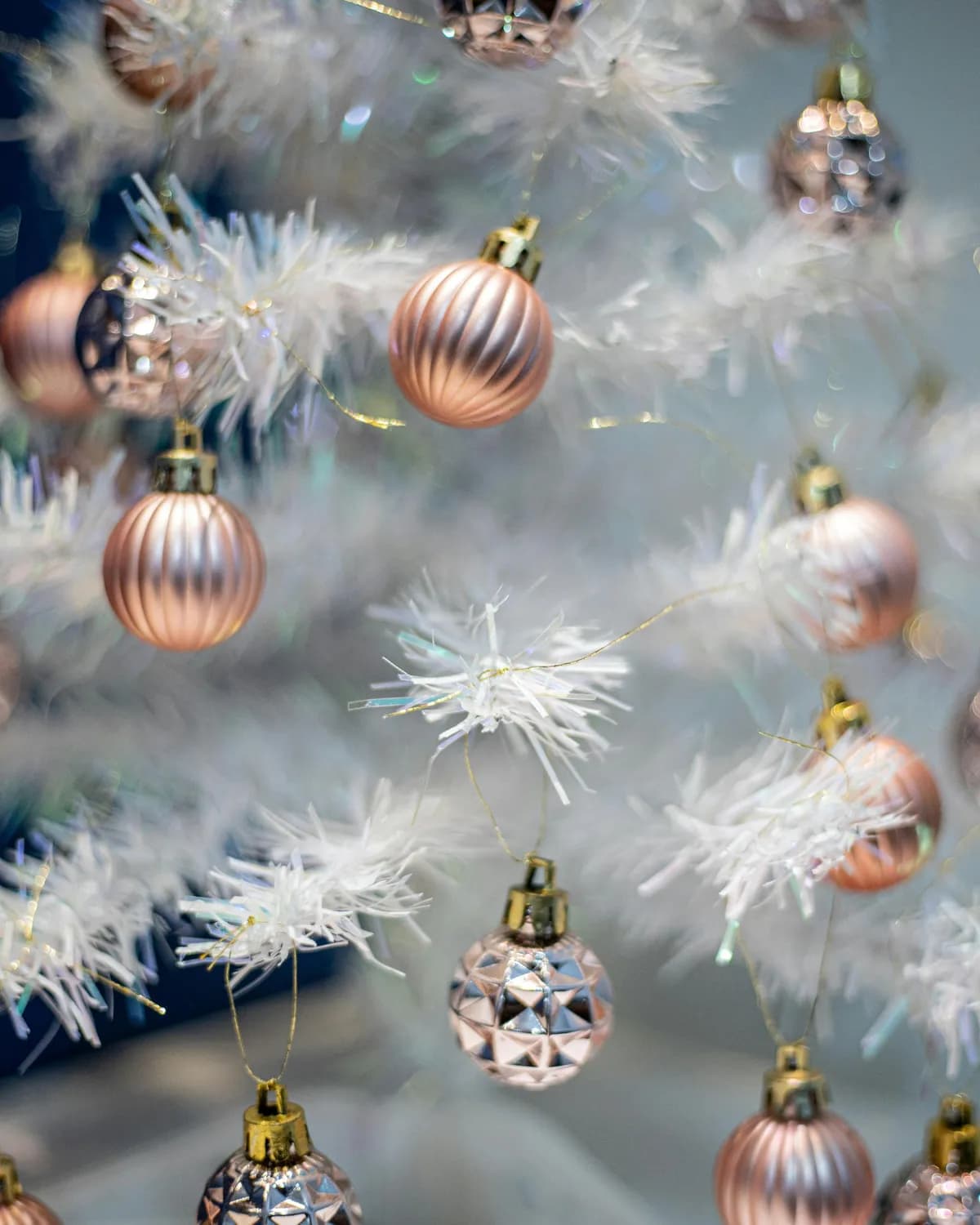 Pormenor de uma árvore de Natal branca decorada com bolas brilhantes em tons de cobre, rosa e prateado.