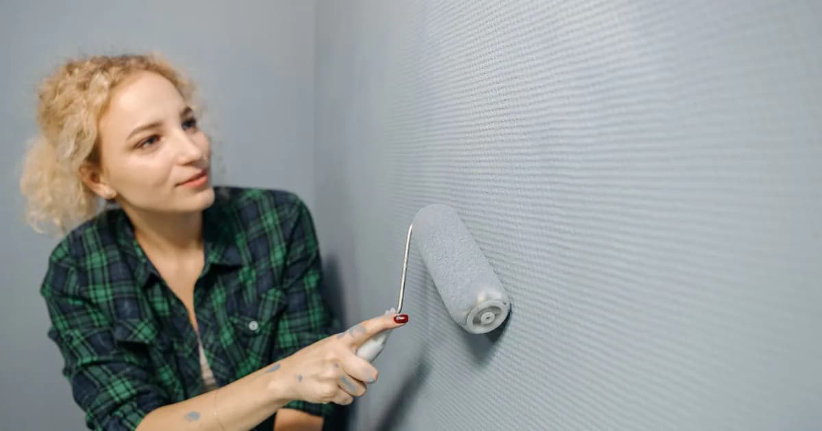 Close view of a woman painting an interior wall with a roller.