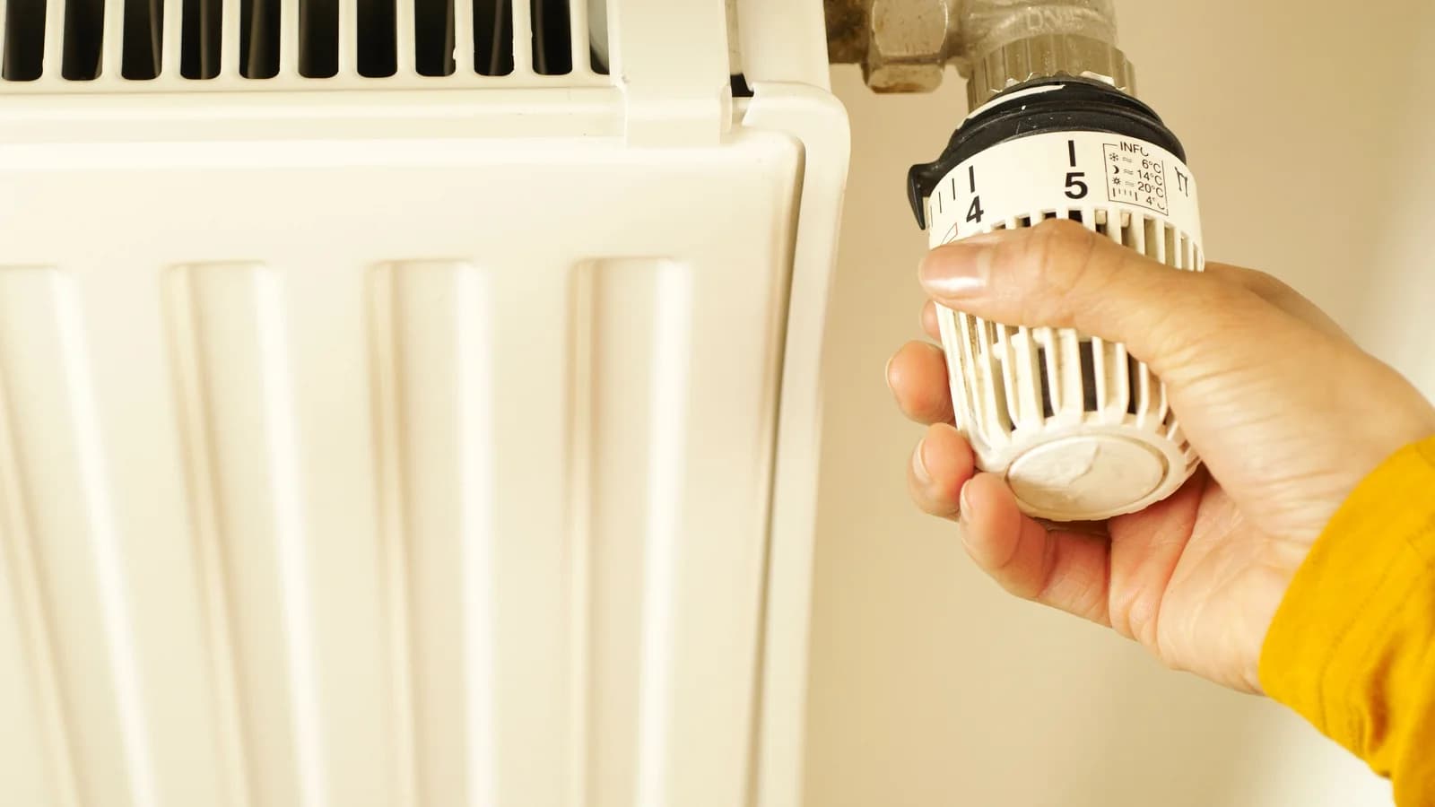 A hand adjusts the thermostatic valve on a white radiator at home.