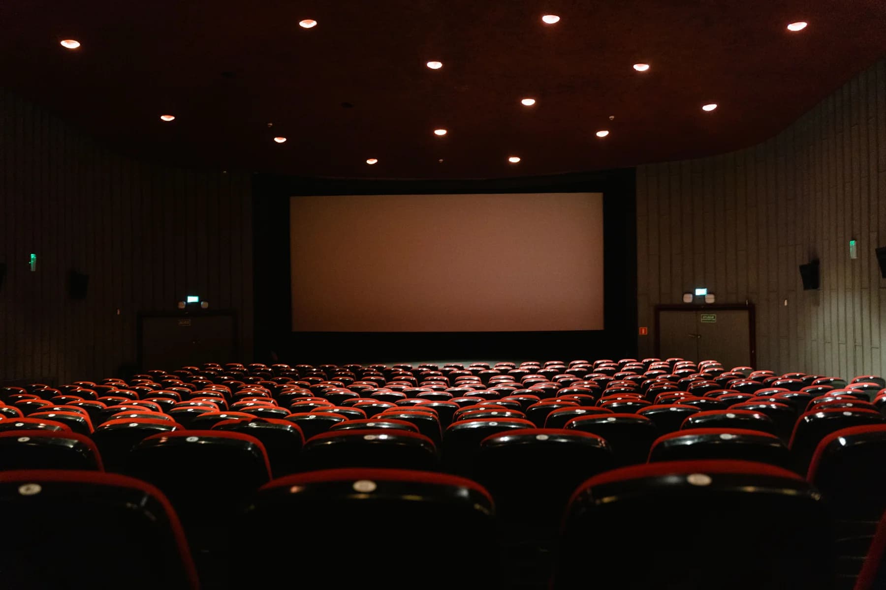 Empty cinema auditorium viewed from the back toward an illuminated screen.