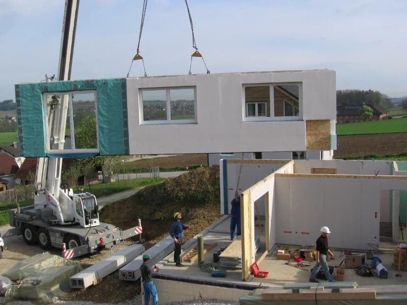 Ein vorgefertigtes Hauselement wird auf einer Baustelle mit einem Kran angehoben.
