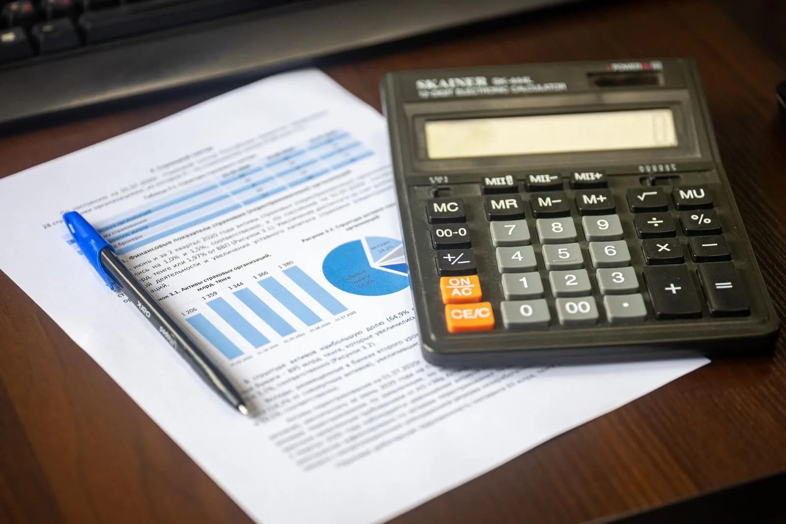 Calculadora e relatório sobre uma secretária, numa cena de análise financeira.