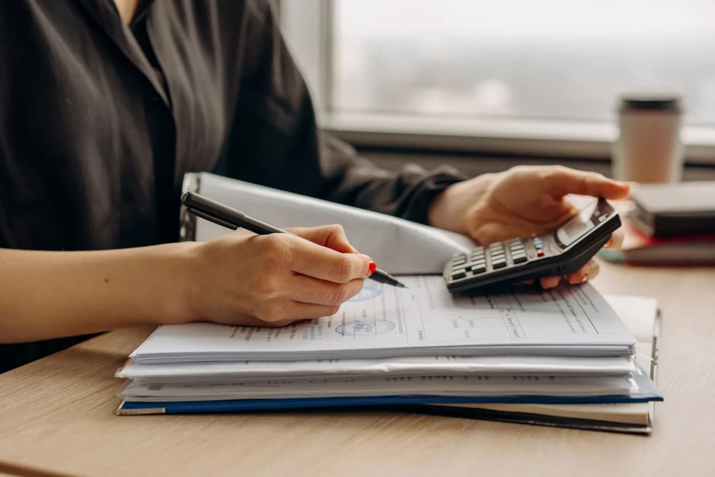 Mãos utilizam uma calculadora sobre documentos durante um cálculo.