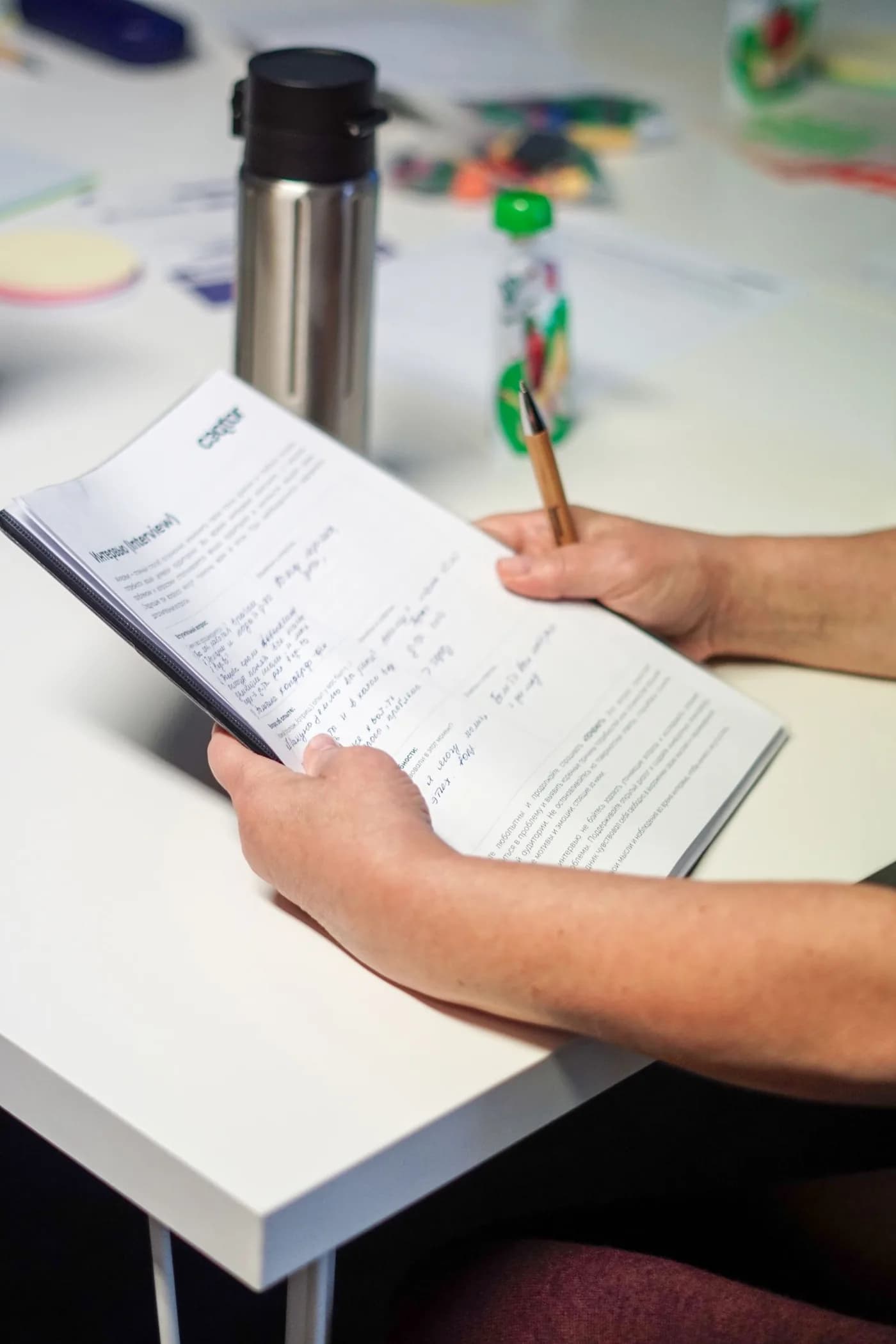 Uma pessoa segura e consulta documentos numa mesa de trabalho.