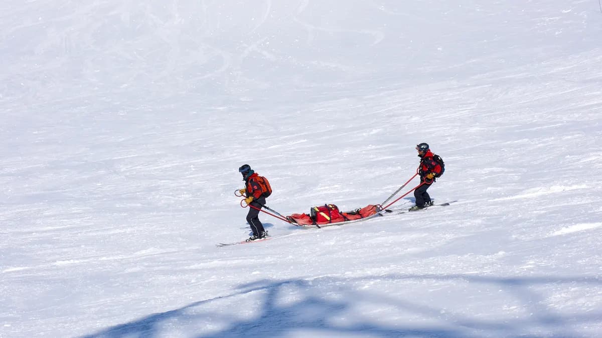 Zwei Retter auf Skiern ziehen einen beladenen Rettungsschlitten über einen verschneiten Hang.